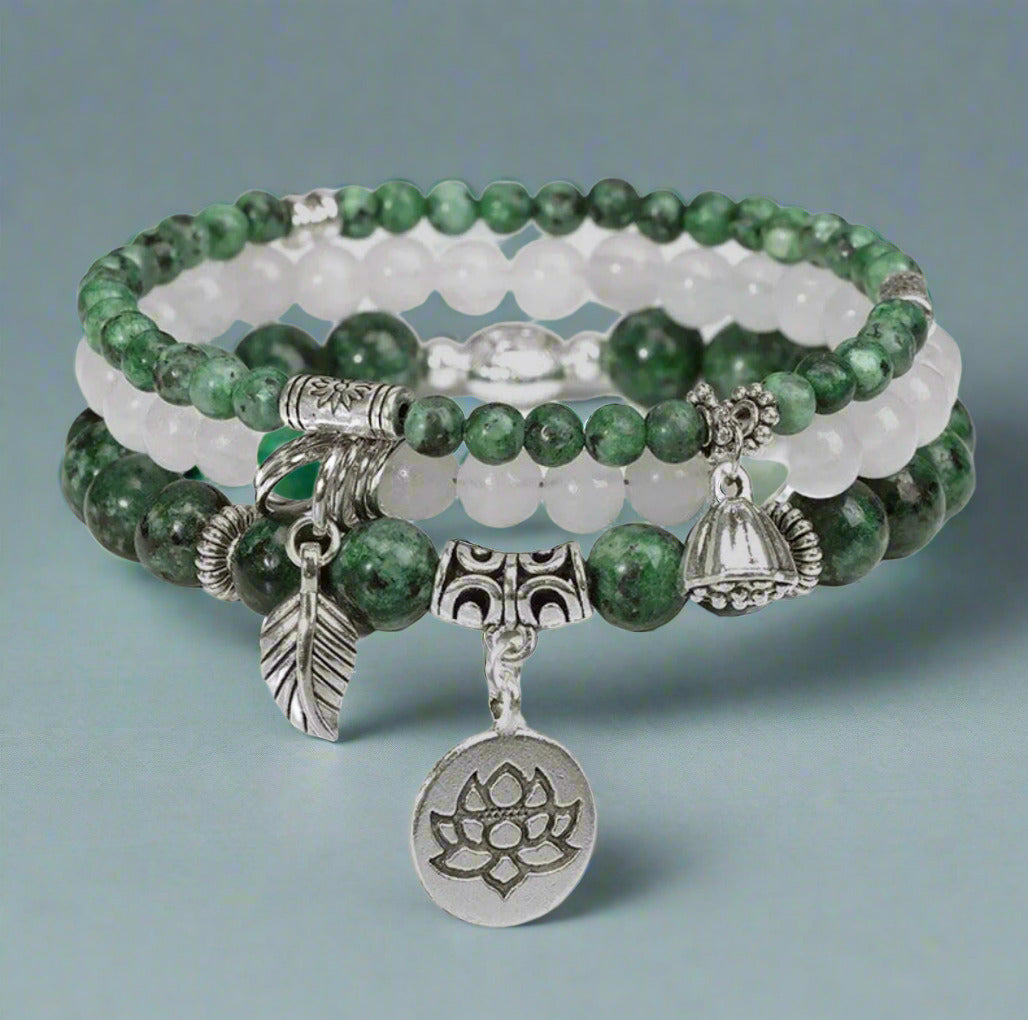 Stack of green and white beaded bracelets with silver charms on a white background