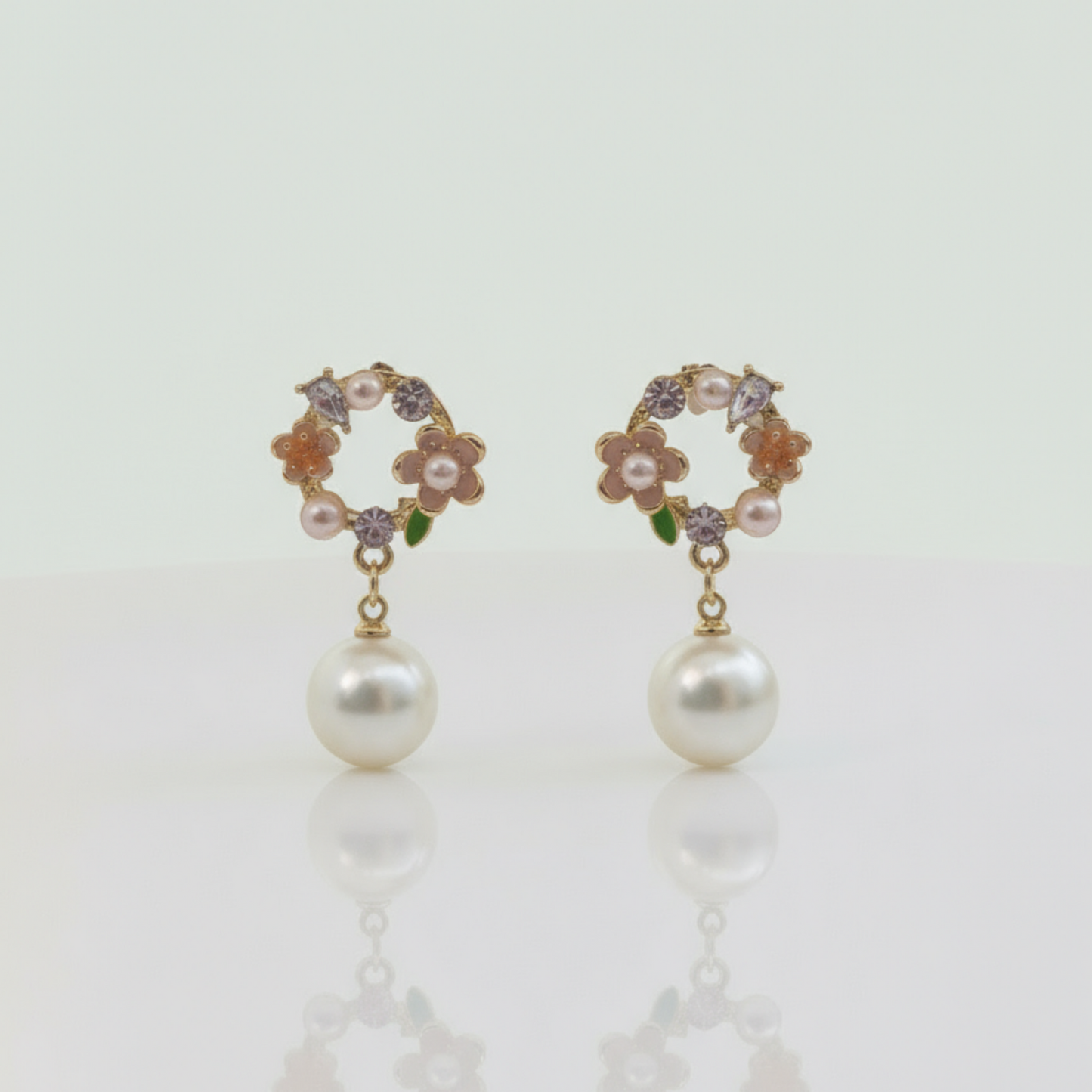 Pair of pearl earrings with floral and gemstone details on a light background