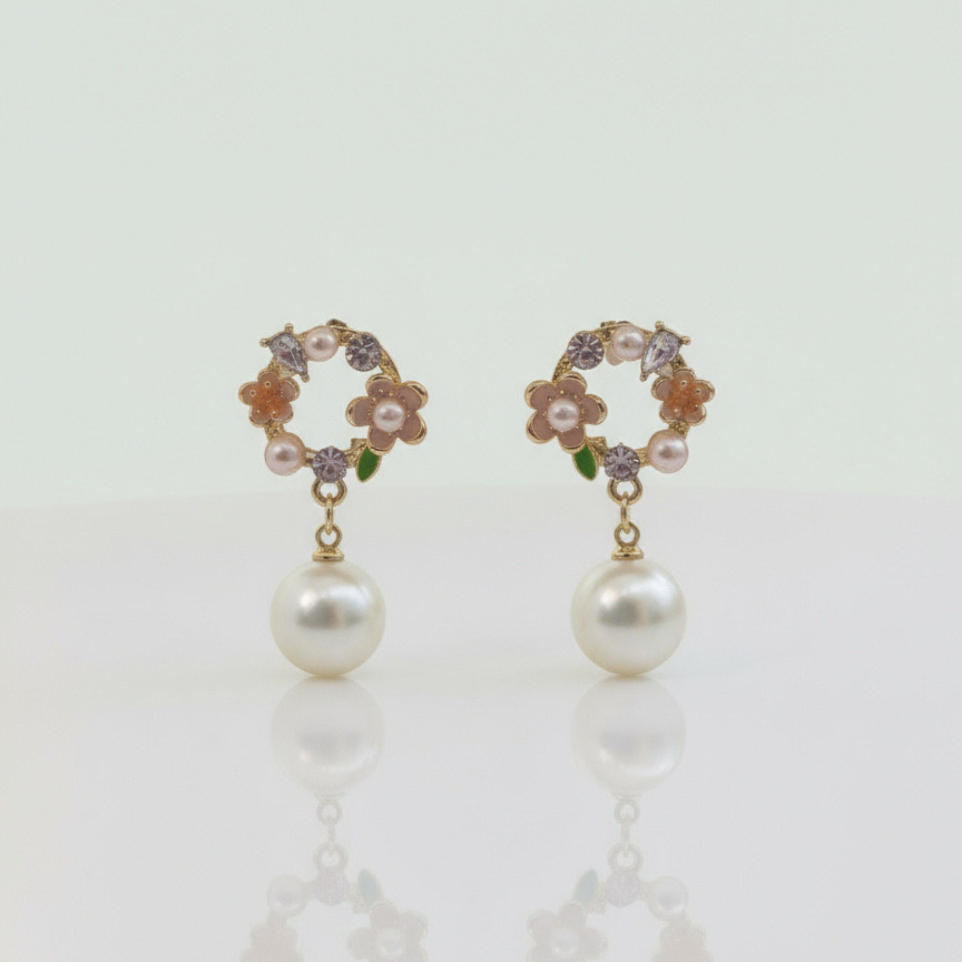 Pair of pearl earrings with floral and gemstone details on a light background