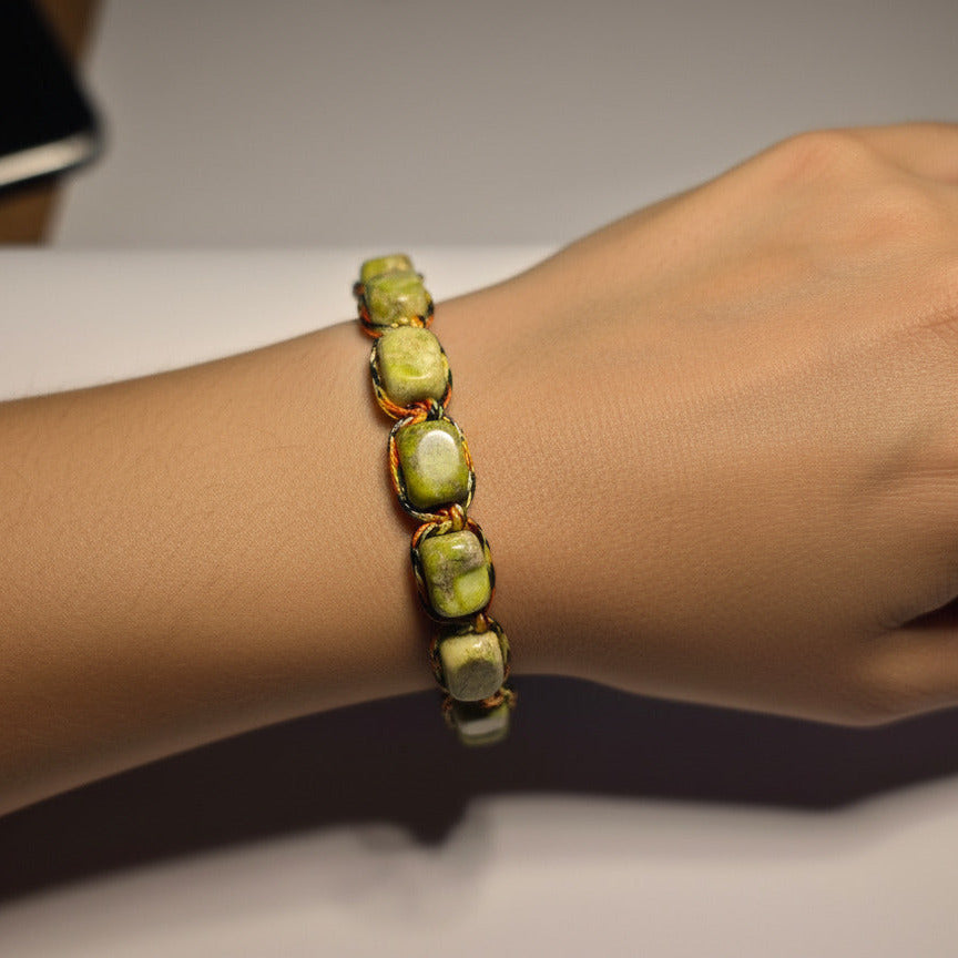 Green beaded bracelet on a white cylindrical object with a blurred background