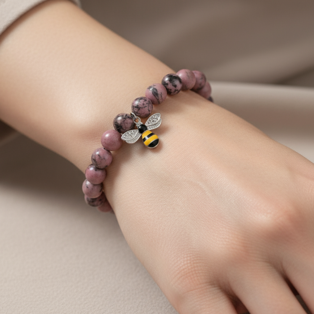 Hand wearing a beaded bracelet with a bee charm on a neutral background