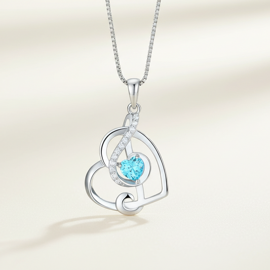 Silver necklace with a heart-shaped pendant featuring a blue gemstone on a light blue background.