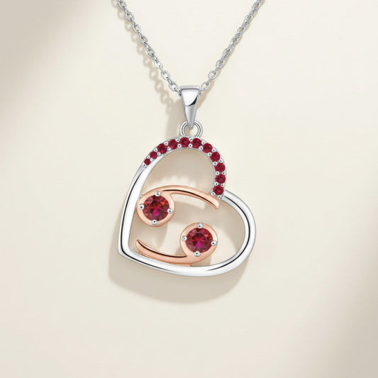 Heart-shaped pendant with cancer zodiac design and red gemstones on a white background